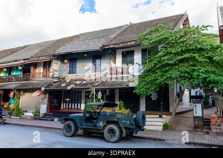 Luang Prabang, Laos - 28. Juni 2020: Traditionelle zweistöckige Gebäude mit Holzbalkonen, Beschilderung für Pensionen und ein Café sowie ein geparkter Jeep im Militärstil sind entlang einer Straße in Luang Prabang zu sehen. Stockfoto