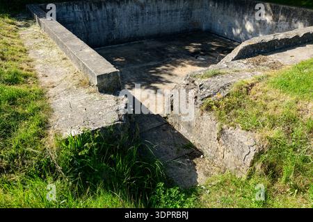 Batterien Hillman, Frankreich - 1. Juni 2021: Das Bild zeigt die Überreste einer Betonpistole mit teilweise versunkenen Mauern und einem offenen Innenraum, umgeben von Gras und Vegetation. Stockfoto
