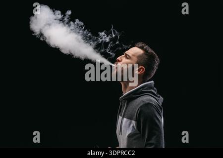 Der Mensch atmet eine große Wolke aus Dampf aus, während er in einem dunklen Raum steht Stockfoto