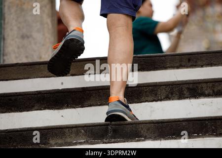 Männlicher Tourist in grauen und orangefarbenen Turnschuhen, die Treppen hinauf gehen, männliche Beinhaut, Blick aus einem hohen Winkel Stockfoto