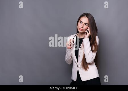 Geschäftsfrau, die telefoniert, während sie eine Brille in einem Studio mit grauem Hintergrund hält Stockfoto