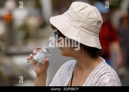 BANGKOK, THAILAND-21. JAN 2026: Weibliche Touristen in Creme Hut Trinkwasser aus der Flasche, weibliche Touristen erkunden Wat Thai, Nahaufnahme Stockfoto