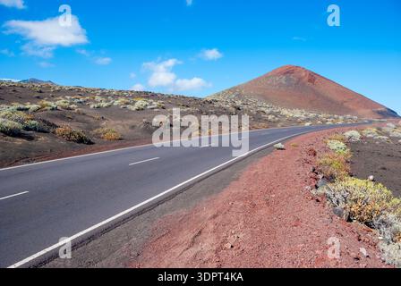 Asphaltstraße, die sich durch eine vulkanische Landschaft mit rötlichem Schlackenkegel unter blauem Himmel schlängelt, El Hierro, Kanarische Inseln, Spanien Stockfoto