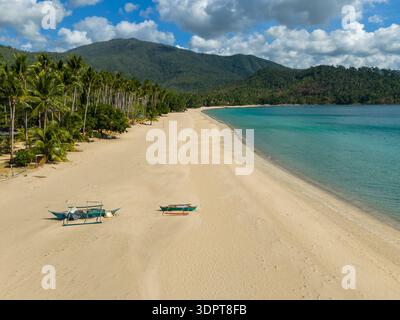 Blick aus der Vogelperspektive auf einen breiten Sandstrand mit zwei kleinen traditionellen Booten, die am Ufer neben ruhigem türkisfarbenem Wasser liegen. Stockfoto