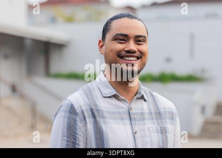 Asiatischer Mann, der im Innenhof steht und kariertes Hemd trägt, Geländer neben Pflanzgefäßen und Steintreppen hält Stockfoto