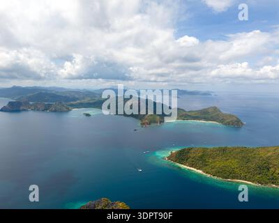 Ein Blick aus der Vogelperspektive zeigt bewaldete Inseln, umgeben von ruhigem blauem Meer mit flachem türkisfarbenem Wasser entlang der Sandküste. Stockfoto