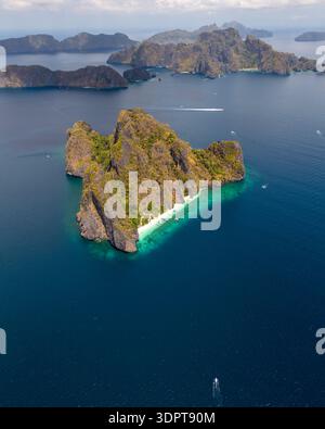 Ein Blick aus der Vogelperspektive zeigt eine steile Kalksteininsel mit freiliegenden Felswänden und einen schmalen weißen Sandstrand, umgeben von klarem türkisfarbenem Wasser. Stockfoto