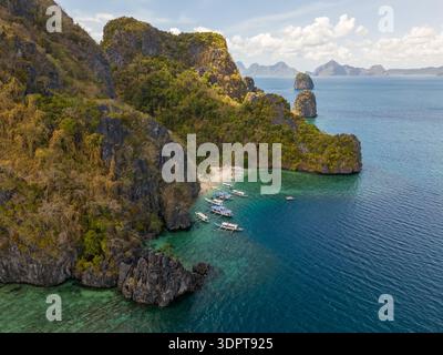 Eine schräge Aussicht aus der Luft zeigt Cudugnon Beach, der unter steilen Kalksteinklippen entlang einer geschützten tropischen Bucht mit klarem türkisfarbenem Wasser liegt. Stockfoto