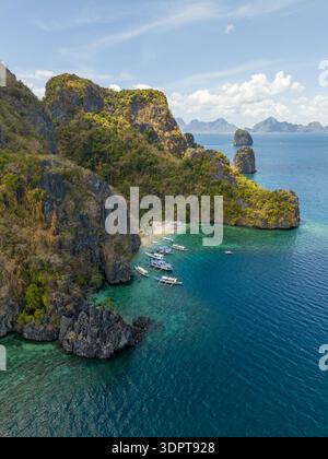 Eine schräge Aussicht aus der Luft zeigt Cudugnon Beach unter steilen Karstkalksteinfelsen entlang einer geschützten tropischen Bucht mit klarem türkisfarbenem Wasser. Stockfoto