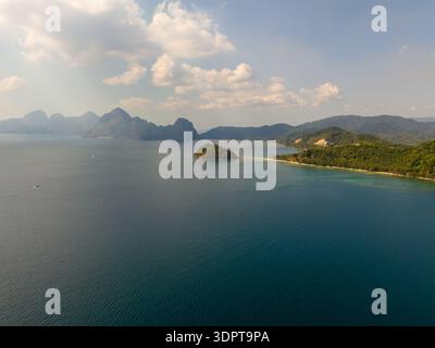 Aus der Vogelperspektive auf eine tropische Bucht mit bewaldeter Küste, Sandstrand und ruhigem blauem Wasser in der Nähe des Las Cabañas Strandes in El Nido. Stockfoto
