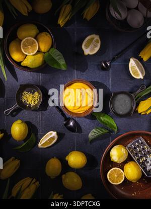 Frische Zitronen, Schale, Eiweiß und cremiger Zitronenquark auf dunklem Hintergrund, mit Zutaten für ein köstliches Dessert, umgeben von lebendigem Gelbtönen Stockfoto
