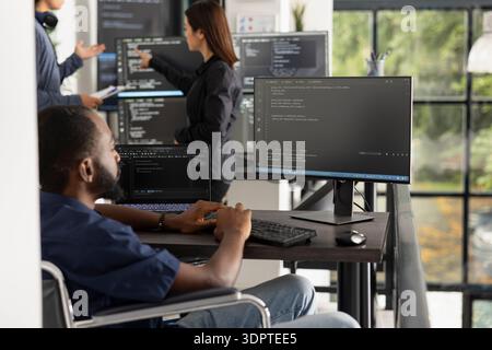 Der schwarze männliche Softwareentwickler sitzt an der Workstation im Büro und konzentriert sich auf die Programmierung von Computern. Motivierter Fachmann in der Technologiebranche hebt die Inklusion von Behinderungen, den Ehrgeiz und die digitale Produktivität hervor. Stockfoto