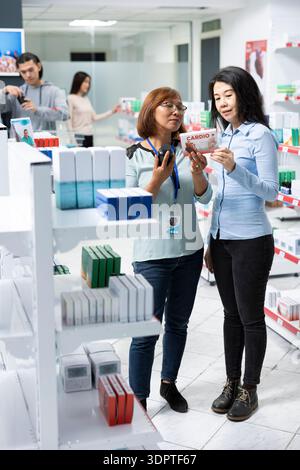 Die Apotheke spricht mit dem Kunden und erklärt die unterschiedlichen Marken von Medikamenten, die für die Behandlung der Herzerholung geeignet sind. Pharmazeutischer Mitarbeiter, der Beratung zu verschiedenen pharmazeutischen Produkten gibt. Stockfoto