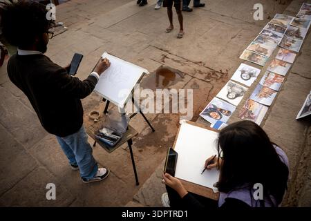 In einem hohen Winkel werden zwei Straßenkünstler erfasst, die Porträts auf den Steinstufen von Dashashwamedh Ghat in Varanasi, Indien, skizzieren. Stockfoto