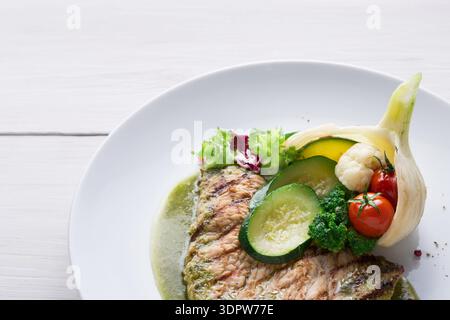 Frischer gegrillter Fisch mit Gemüse auf einem weißen Teller im Restaurant Stockfoto