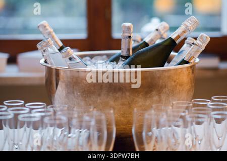 Champagner- und Wasserflaschen, gekühlt im Eiskübel mit leeren Gläsern Stockfoto