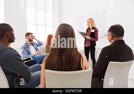Gruppe von Personen, die während der Tageszeit an einer Präsentation in einem hellen Raum teilnehmen Stockfoto