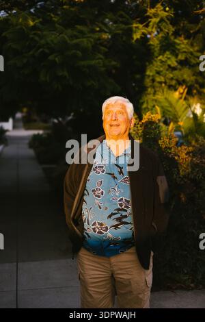 Älterer Mann mit grauen Haaren in strahlendem Sonnenschein und hawaiianischem Hemd Stockfoto