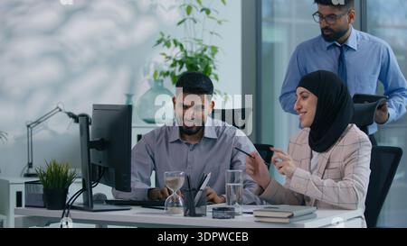Drei Geschäftskollegen. Geschäftsmann mit islamischer Geschäftsfrau diskutieren über reden, arbeiten, Computer aussehend, Arabisch-Mann-Chef kommt ins Amt Stockfoto