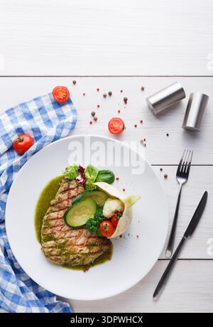 Gegrillter Lachs, serviert mit Gemüse und Kräutern auf einem weißen Teller und einer Serviette mit blauem Karomuster Stockfoto