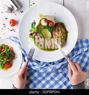 Köstlicher gegrillter Fisch, serviert mit Gemüse und Sauce auf einer sauberen weißen Platte zur Mittagszeit Stockfoto