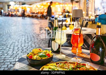 Ein Tisch für einen klassischen italienischen Aperitivo während des Sonnenuntergangs in einer urbanen Umgebung im Freien. Die Szene umfasst Gläser erfrischendes Spritz und Hugo cockta Stockfoto