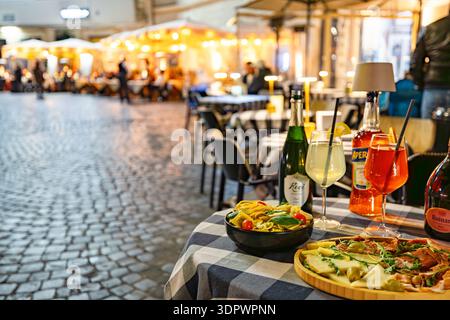 Rom, Italien - 14. Februar 2026: Tisch für einen traditionellen italienischen Aperitivo auf einem malerischen römischen Platz in der Abenddämmerung. Die Szene zeigt eine Brille von A Stockfoto
