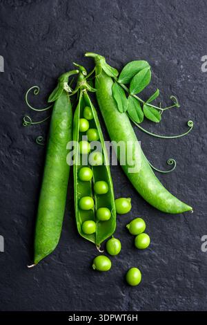 Grüne Erbsen in Schoten auf schwarzem Hintergrund in der Draufsicht. Einfache rustikale Gemüsekost-Komposition Stockfoto