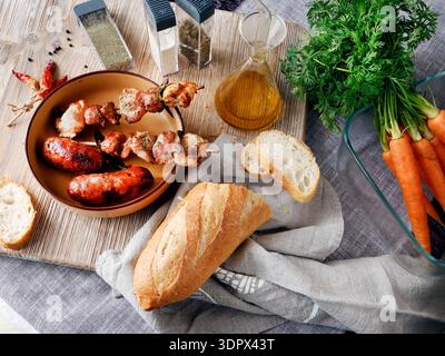 Zusammensetzung von Grillwürsten und Fleischstücken auf Holzspießen. Saisonale Bauernprodukte, Gemüse und Brot. Hausgemachte Speisen. Designer-Hintergrund. Stockfoto
