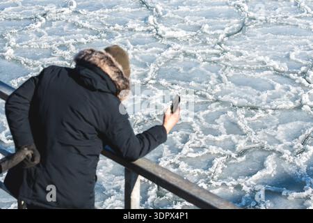 Person, die ein Foto von schwimmendem Meereis und verstreuten Eisschollen macht, die abstrakte Muster auf kaltem Wasser bilden und einen strukturierten Winterhintergrund schaffen Stockfoto