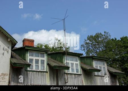 Rustikale Dachfenster sind in einem Holzgebäude mit grünen Zierleisten und Wellblechdach sichtbar. Eine schlanke TV-Antenne erhebt sich in der Mitte. Stockfoto