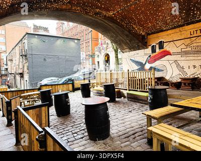 Manchester, Großbritannien - 24. Januar 2026: Die gemütliche, urbane Terrasse von O'Connell in Manchester verfügt über Holztische, Fässer und ein farbenfrohes Wandgemälde. Stockfoto