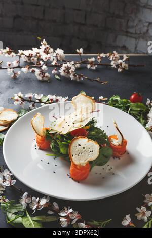 Salat mit Lachs und knusprigem Brot serviert auf einem weißen Teller mit Blumen im Hintergrund Stockfoto