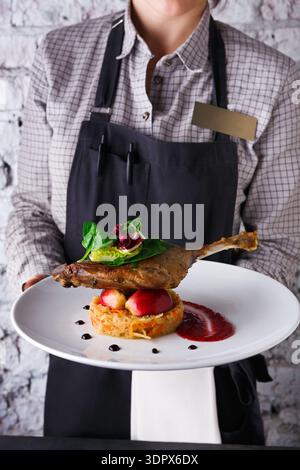 Der Kellner serviert Entengericht mit Gemüse und Sauce in einem Restaurant an einem geschäftigen Abend in der Stadt Stockfoto