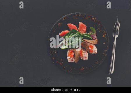 Fischgericht auf schwarzem Teller mit grünen und Grapefruitscheiben vor dem Abendessen Stockfoto