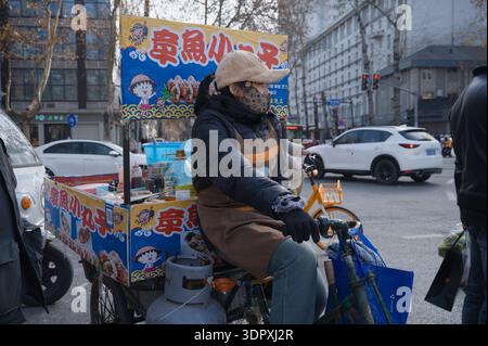 Weibliche Verkäuferin auf einem dreirädrigen Lebensmittelwagen, die Takoyaki an einer geschäftigen Kreuzung in Xi'an verkauft Stockfoto
