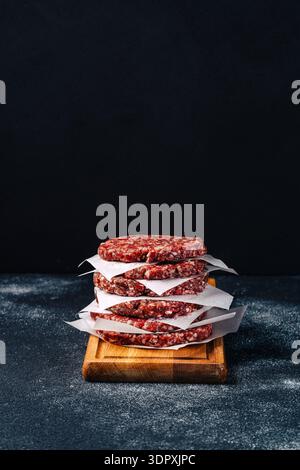 Ein Stapel Kalbsburger-Patties, getrennt durch Pergamentpapier, sitzt auf einem Holzbrett. Die reiche, marmorierte Textur der Patties wird vor einem da präsentiert Stockfoto