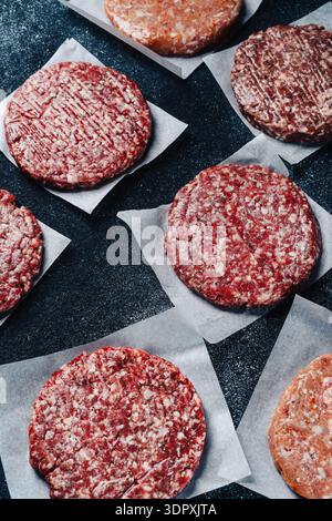 Frische, rohe Kalbsburger-Patties, ordentlich auf Pergamentpapier angeordnet, bereit zum Grillen oder Kochen, auf dunklem Hintergrund für einen auffälligen Betrug Stockfoto