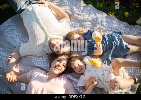 Eine glückliche Familie von vier Personen, darunter ein Mann, eine Frau und zwei Mädchen, feiert fröhlich Ostern. Sie liegen draußen auf einer Picknickdecke und genießen die Stockfoto