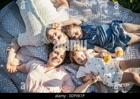 Eine glückliche Familie von vier Personen, darunter ein Mann, eine Frau und zwei Mädchen, feiert fröhlich Ostern. Sie liegen draußen auf einer Picknickdecke und genießen die Stockfoto