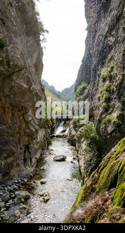 Bergschlucht mit Fluss und kleiner Staumauer entlang der Ruta del Cares in Asturien, Spanien. Dramatische Kalksteinklippen und fließendes Wasser schaffen eine malerische Natur Stockfoto