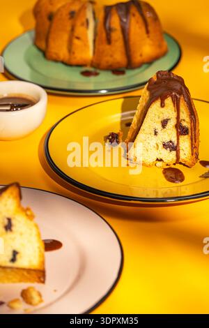 Eine herrliche hausgemachte Biskuitscheibe mit üppigem Schokoladennebel. Der feuchte Kuchen liegt auf einem leuchtend gelben Teller und schafft so eine verlockende Bäckerei Stockfoto
