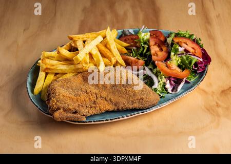 Eine köstliche Portion traditioneller Cachopo, begleitet von knusprigen goldenen Pommes frites und einem frischen Salat mit Salat, Tomaten und Zwiebeln, präsentiert auf einem Tag Stockfoto