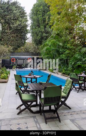 Eine ruhige Terrasse am Pool mit grünen gepolsterten Holzstühlen und Tischen neben einem klaren blauen Pool, umgeben von dichten tropischen Pflanzen und hohen tischen Stockfoto