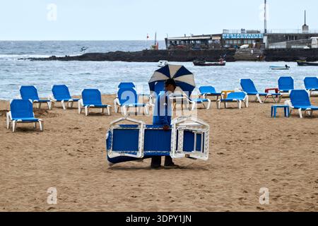 Mann packt Liegen und Sonnenschirme am Ende des Tages playa de las canteras las palmas de gran canaria, kanarische Inseln, spanien Stockfoto
