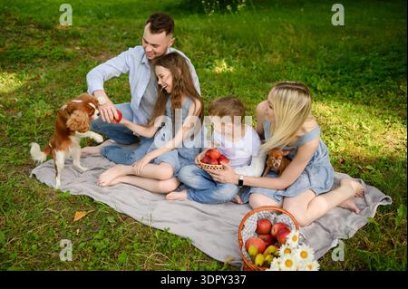 Familie genießt erholsamen Urlaub in der Natur, sitzt auf einer Decke und spielt mit Tieren im Freien. Entspannender Sommertag in der Natur, mit Eltern und Chill Stockfoto
