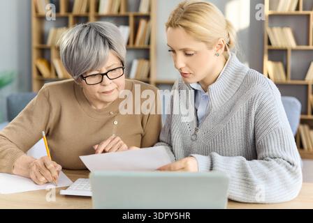 Junge Frau, die älteren Müttern hilft, Rechnungen und Budgets mit einem Laptop zu Hause zu verwalten Stockfoto