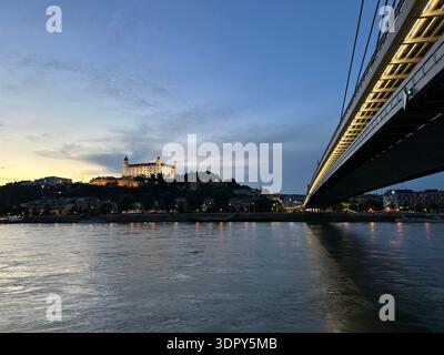 Beleuchtete Burg Bratislava in der Abenddämmerung mit der SNP-Brücke über die Donau, Slowakei, Mai 2024 Stockfoto