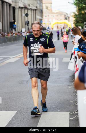 Ein entschlossener Läufer mittleren Alters, der ein dunkelblaues CUS Parma Shirt und Startnummer 369 trägt, läuft mit einem Gelb durch die Straßen von Parma Italien Stockfoto