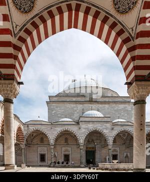 Weitwinkelblick auf den historischen Innenhof der osmanischen Moschee mit gestreiften Bögen und hohen Minaretten unter bewölktem Himmel in Edirne, Türkei. Stockfoto